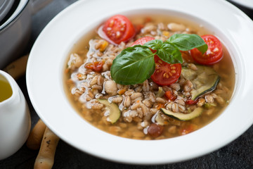 White plate with italian soup made of spelt and vegetables, close-up, selective focus