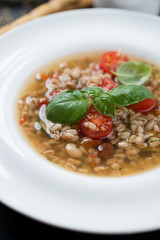 Closeup of a white plate with spelt and vegetable soup, selective focus, vertical shot