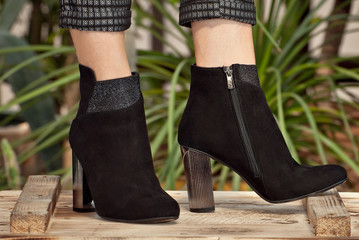 Black suede shoes for women's leg. The girl walks in shoes. Classic shoes on the background of tropical plant arranger.