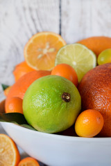 Citrus assortment in a bowl against the white wooden background. Red orange, lime, lemon and kumquats