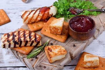 Grilled adyghe cheese, crackers, red jam, spices and cress salad on the wooden board against the white background