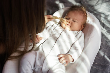 Mother with her newborn son on the bed in the rays of sunlight coming out of the window. Baby lies...