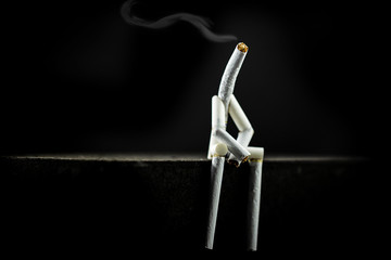 image of a character made of cigarette, alone and sad with black background. Concept of addiction...