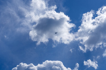 The plane flies against the blue sky with clouds