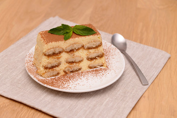 Tiramisu cake with coffee and fresh mint, on a plate on a light wooden background. Selective focus.