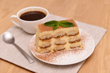Tiramisu cake with coffee and fresh mint, on a plate on a light wooden background. Selective focus.