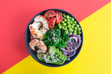 Poke bowl with red shrimps and vegetables in the dark bowl in the center of the colorful  background.Top view.Closeup.