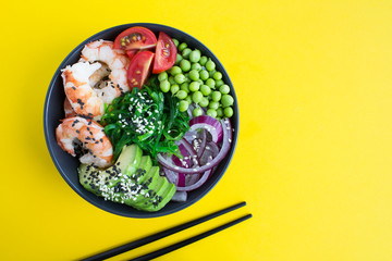 Poke bowl with red shrimps and vegetables in the dark bowl on the yellow background.Top...