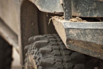 Wheels, lights and bumper are laced in a swamp. Dirty parts of a truck close up.