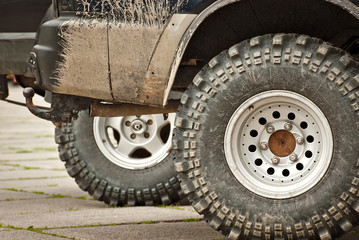 Wheels, lights and bumper are laced in a swamp. Dirty parts of a truck close up.