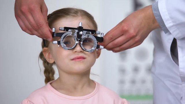 Optometrist putting phoropter on little girl, child complaining to see nothing