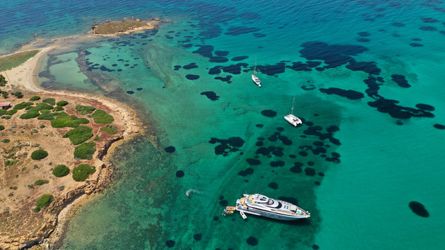 Aerial drone bird's eye view of small islet of Ydrousa with turquoise and sapphire clear waters and only one mile distance from coast in Voula, Athens riviera, Attica, Greece