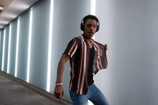 attractive young handsome guy walks in the neon light of the night city listens to music in wireless headphones from a mobile phone and dances fun