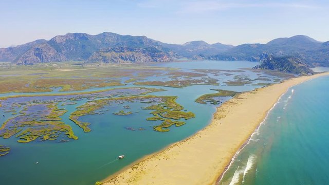 Aerial survay over the river Dalyan. Iztuzu Sand Spit separates the river and the sea. Tourist boat sailing on the river. Birds eye view 4k
