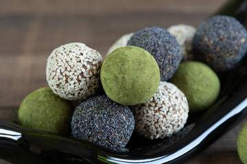 Handmade energy balls with poppy, sesame and matcha tea in recycled green bottle on dark wooden background. Close up