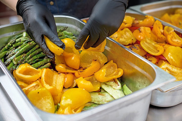 Grilled vegetables in a large container in the kitchen, the cook interferes with the hands of...