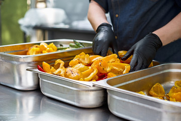 Grilled vegetables in a large container in the kitchen, the cook interferes with the hands of...