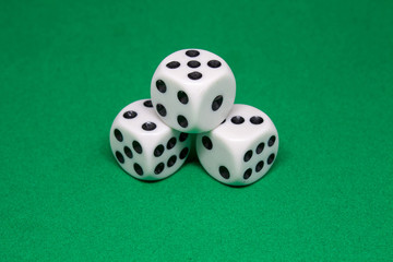 Three white playing dice lie in the form of a pyramid on a green playing table close-up 