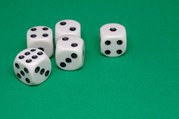 Five white playing dice lie in a group on a green playing table close-up