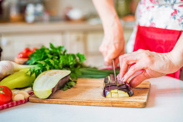 Female hand with knife cuts eggplant on board in kitchen. Cooking vegetables