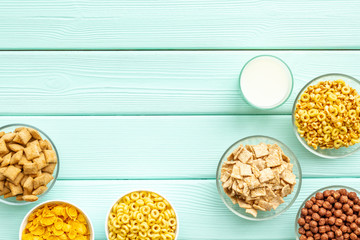 Various corn cereals in bowls and milk on mint wooden background top view copyspace