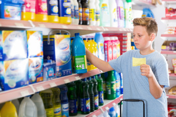 Serious preteen boy choosing household chemicals on shopping list