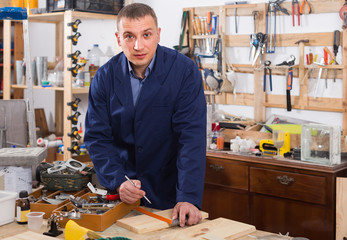 Portrait of young handsome carpenter in uniform in workshop.