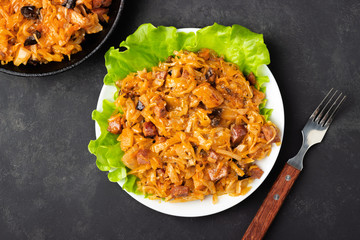 Traditional dish of polish cuisine - Bigos from fresh cabbage, meat and prunes. Top view. Dark background.