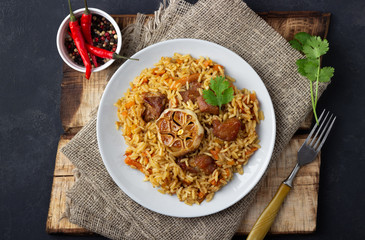 Oriental cuisine. Uzbek pilaf or plov from rice and meat in a cast iron pan on wooden rustic board. Top view.