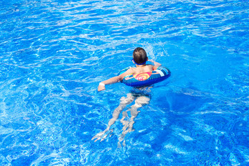 Happy cute little boy lying on an circle in the swimming pool. Cool summer holidays for children and kids. Active games on the water.