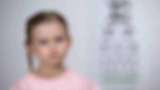 Little girl squinting eyes, suffering blurred vision, diagnostics of astigmatism
