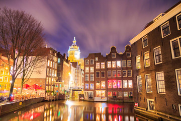 Blurred dramatic night sky over traditional historical buildings on a canal, by the Armbrug bridge, in Amsterdam, Netherlands, with the Basiliek van de Heilige Nicolaas (Church of Saint Nicholas).