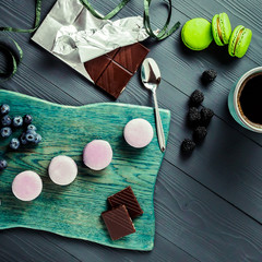 FRENCH CAKES MACARONS CURRANT BLUEBERRY MINT ON WOODEN BOARD WITH COFFEE CUP AND CHOCOLATE ON WOODEN GRAY BACKGROUND