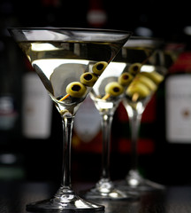 Three Martini drinks with olives on stick in club on black table