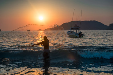 Fototapeta premium Silhouette of fisherman boy at sunset on the beach and boat background