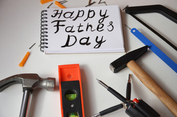 Happy Father's Day inscription with work tools on white background. Greetings and presents