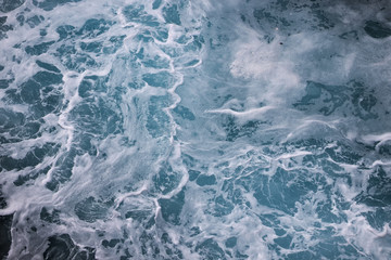 Fototapeta na wymiar blue ocean waves creating white foam seen from above.