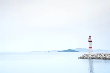 Fotobehang Lonely lighthouse on a stone road in the middle of the sea with views of the mountains and fog, Turgutreis Turkey © YuliiaMazurkevych
