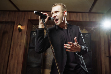 Portrait of handsome attractive singer singing hit with open mouth in microphone.