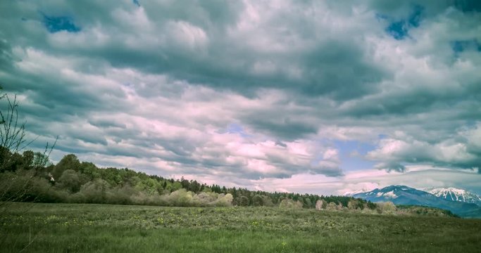 Time lapse of dark clouds above a grassy field in the countryside, with snow covered mountains in the distance.