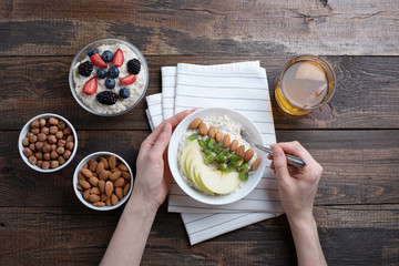 Top view of women's hands at Breakfast, oatmeal with almonds and Apple, nuts, berries, compote
