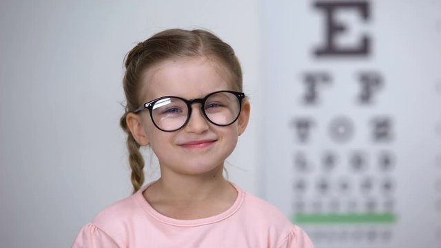 Optician putting glasses on little girl and making her happy, professional help