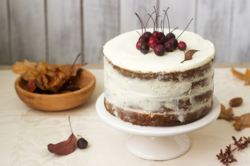 Apple cake with cream, decorated with small apples against the background of autumn composition. Rustic style.