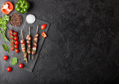 Grilled pork and chicken kebab with paprika on stone chopping board with salt, pepper and tomatoes on black background. Fresh lettuce and paprika pepper. Top view. Space for text - Powered by Adobe