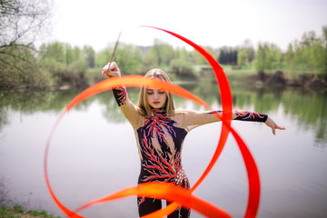 Rhythmic gymnastics. Young gymnast girl with red ribbon outdoor in park