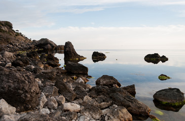 Fototapeta na wymiar Boulders and rocks in the water. Beautiful seashore with different stones. Blue sky with clouds reflection in water. Nature composition. 