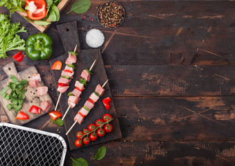 Raw pork kebab with paprika on chopping board with fresh vegetables and disposable charcoal grill on wooden background with fork and knife. Salt and pepper with lettuce. Space for text