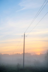 Power transmission line supporting structure at sunrise in the fog