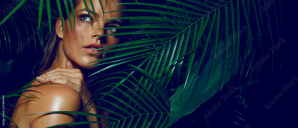 Wall mural a beautiful tanned girl with natural make-up and wet hair stands in the jungle among exotic plants