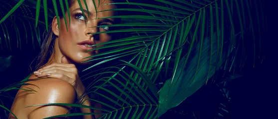 Abwaschbare Fototapete Frauen Ein wunderschönes gebräuntes Mädchen mit natürlichem Make-up und nassen Haaren steht im Dschungel zwischen exotischen Pflanzen